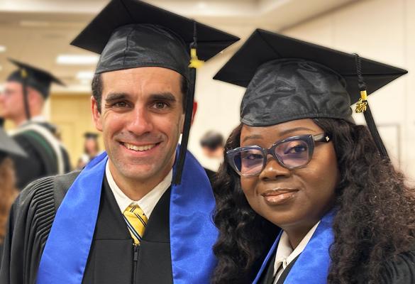 Deux diplômés souriants portant toge noire, épitoge bleue et mortier traditionnel en préparation à la cérémonie de collation des grades, d’autres finissantes et finissants en arrière-plan.