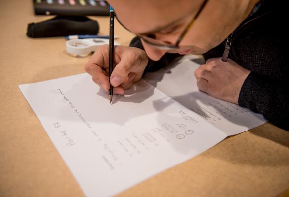 Un étudiant écrit à la main sur une feuille posée sur une table, concentré sur son travail.