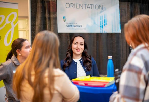 Une orienteuse sourit, accueillant autour d'une table des participantes d'une foire informative.