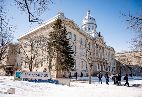 La façade de l'Université de Saint-Boniface un jour ensoleillé d'hiver, des passants sur le trottoir.
