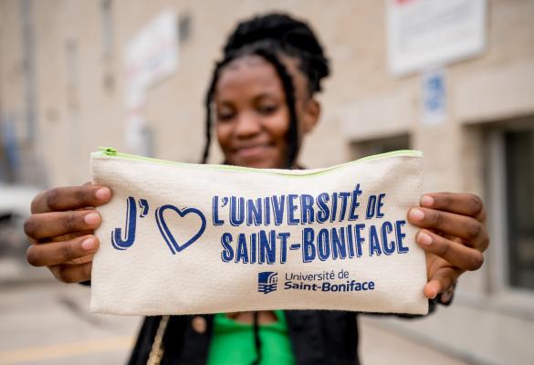 Une étudiante qui tient une trousse avec « J'aime l’Université de Saint-Boniface » écrit dessus.