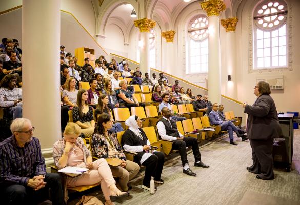 Un auditorium rempli de personnes étudiantes, plusieurs avec un ordinateur sur les genoux, regarde vers l’avant. 