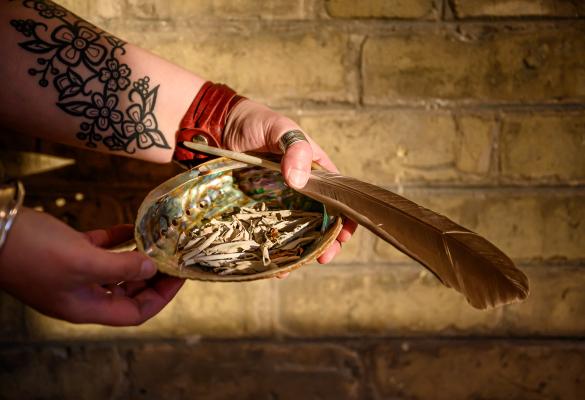 Des mains tenant une plume et de la sauge pour une cérémonie.