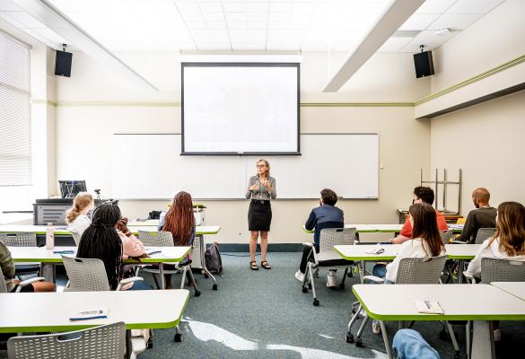 Une enseignante en salle de classe devant un groupe de personnes apprenantes.