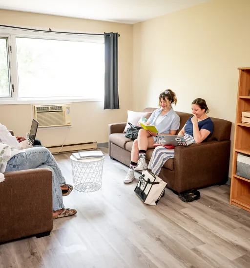Des étudiantes font de la lecture, assises sur un divan dans le salon d'un appartement.
