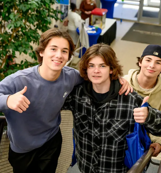 Trois adolescents montant un escalier regardent l’objectif en souriant. Les deux au premier plan lèvent le pouce de la main.   