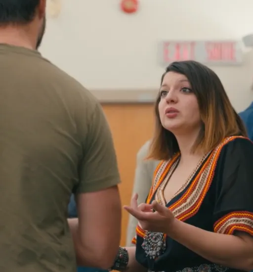 Une femme debout dans une salle de conférence discute avec un homme qui est dos à la caméra.