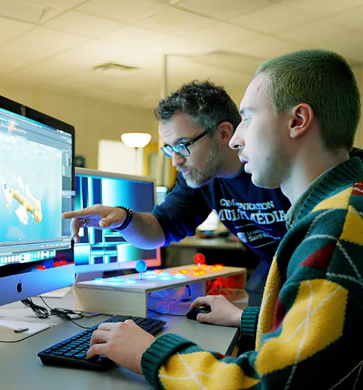 Dans une salle de classe de l'USB, deux personnes regardent un écran d’ordinateur. L’une utilise un clavier et une souris, et l’autre se penche et pointe l’écran.
