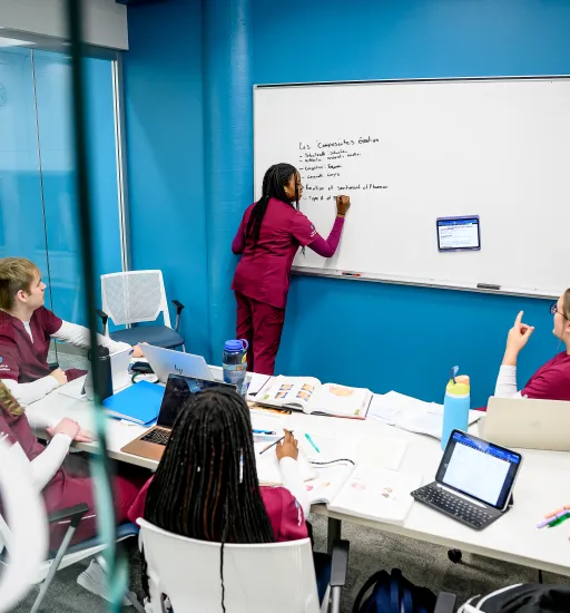 Cinq personnes en vêtements de soins infirmiers revoient leurs notes de cours ensemble dans une salle de travail de groupe à la bibliothèque de l’USB.