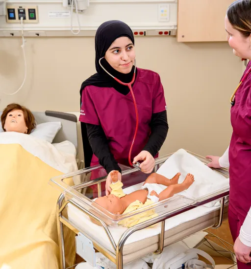 Deux personnes en uniforme dans un contexte hospitalier travaillent avec un mannequin adulte et un mannequin bébé.  