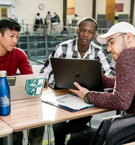 Trois personnes sont assises à une table dans le centre étudiant Étienne-Gaboury de l’USB et regardent un ordinateur.