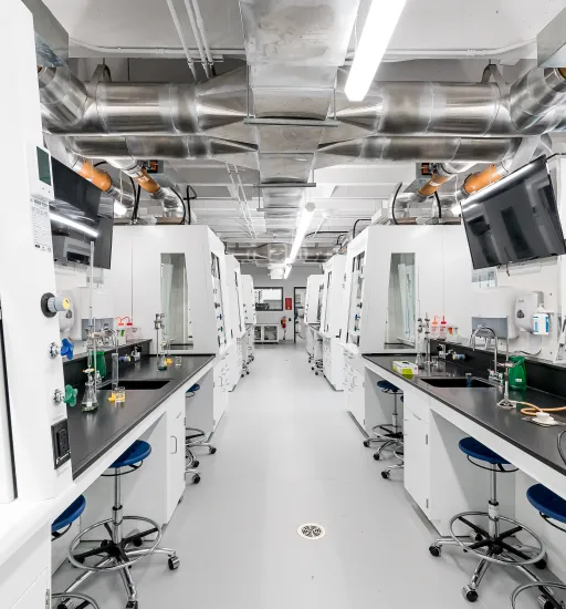 Un grand laboratoire avec deux longs comptoirs noirs entrecoupés de hottes de ventilation, des écrans et des tabourets.