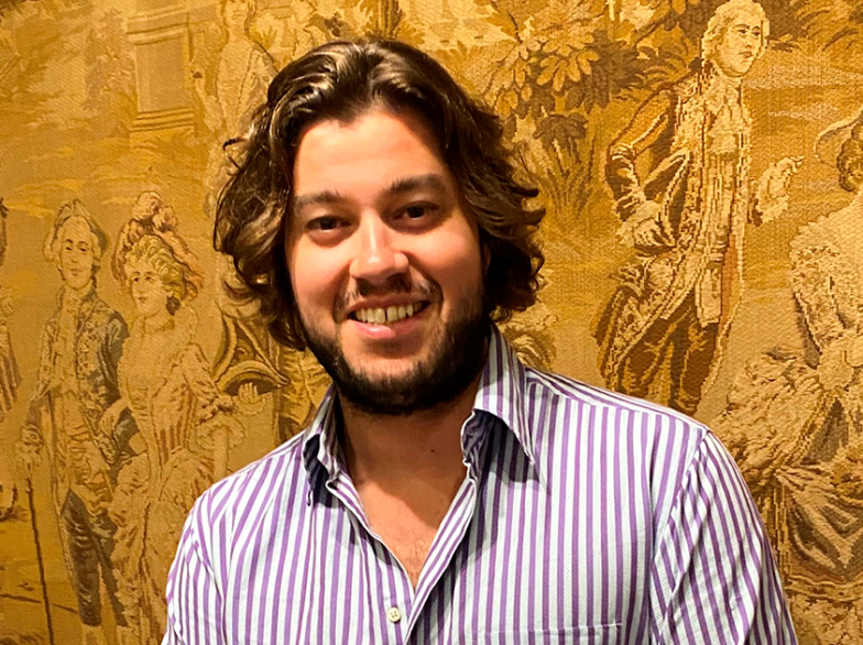 Jérémy Baudet sourit devant une tapisserie, reconnu pour sa contribution aux soins de santé en français au Manitoba.