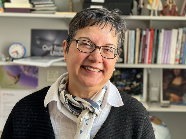 Portrait de Maria Fernanda Arentsen souriante, debout devant une bibliothèque remplie de livres dans son bureau à l’USB.