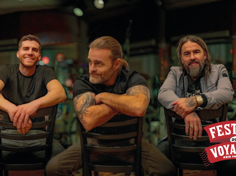 Les trois membres du groupe La Chicane assis à l’envers sur des chaises devant une scène de spectacle. Le logo du Festival du Voyageur 2025, avec les dates du 14 au 23 février.