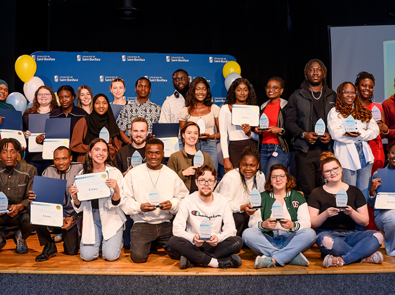 Groupe d’étudiantes et étudiants posant fièrement avec certificats et trophées sur scène à l’Université de Saint-Boniface.