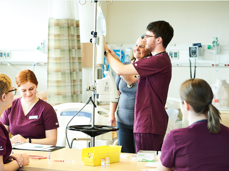Étudiantes et étudiant en tenue médicale effectue des activités pratiques dans un laboratoire de simulation clinique, sous la supervision de profs.