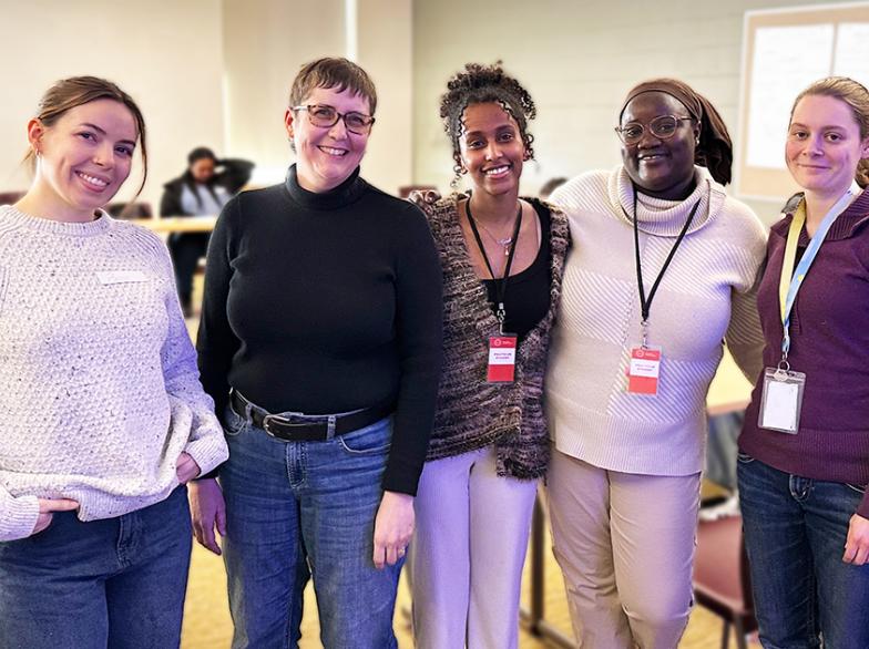 5 étudiantes debout côte à côte sourient pour la prise d'une photo dans une salle de classe.