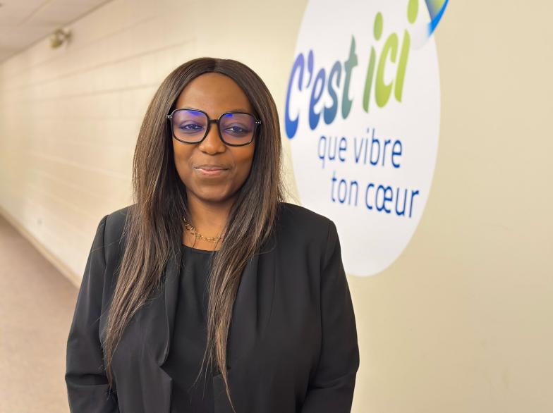 Nathalie Hukportie debout dans un couloir de l'USB, sur une murale derrière elle est écrit « C'est ici que vibre ton coeur ».