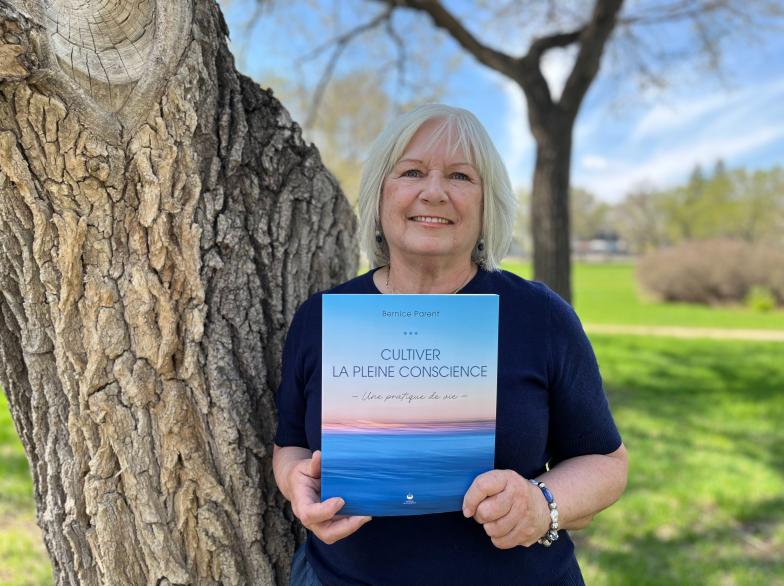 Accotée sur un arbre, Bernice Parent montre fièrement son livre « Cultiver la pleine conscience ».