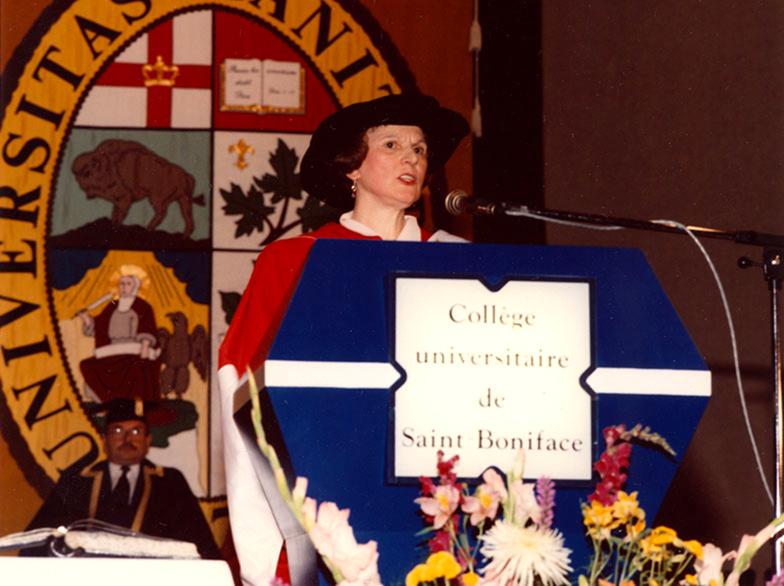 Annette Saint-Pierre, vêtue d'une toge rouge et blanche, livre un discours au podium lors de la collation des grades.