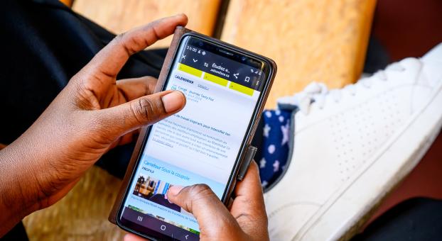 Des mains tiennent un appareil mobile affichant le site web de l'Université de Saint-Boniface.