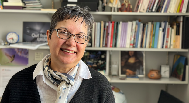 Portrait de Maria Fernanda Arentsen souriante, debout devant une bibliothèque remplie de livres dans son bureau à l’USB.