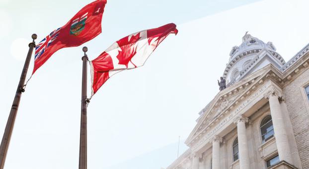 Drapeaux du Canada et du Manitoba flottant devant la façade historique de l’Université de Saint-Boniface.