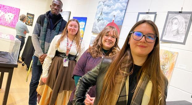 Quatre artistes étudiants posent fièrement devant leurs œuvres exposées à la Galerie de l’USB.