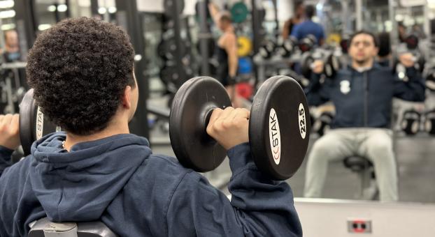 Un homme faisant face à un miroir effectue des développés des épaules avec des poids haltères.