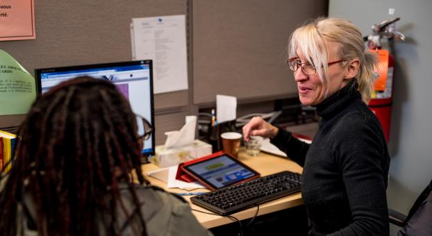 Une tutrice aide une personne étudiante à un bureau avec un ordinateur et une tablette.