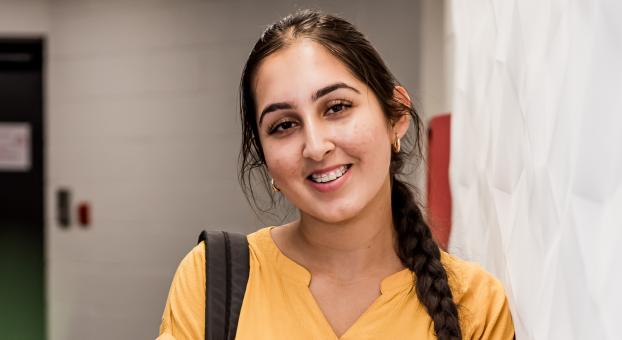 Une étudiante, vêtue d’un chandail jaune et portant un sac à dos, est appuyée contre un mur.