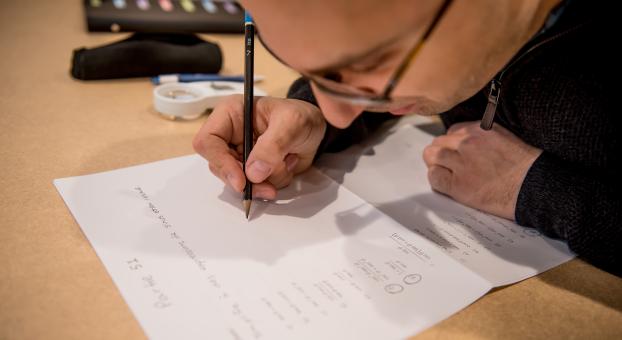 Un étudiant écrit à la main sur une feuille posée sur une table, concentré sur son travail.