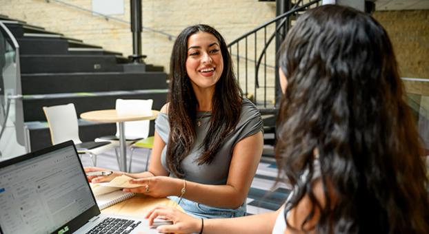 Deux étudiantes échangent autour d’une table dans un espace commun de l’Université Saint-Boniface.