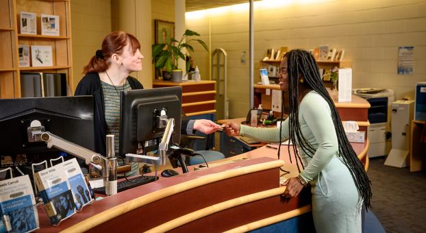 Une employée reçoit le paiement d’une étudiante à un comptoir de l’Université de Saint-Boniface.