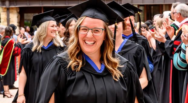Personne en toge au premier plan avançant lors d’une cérémonie de remise des diplômes, entourée d’applaudissements