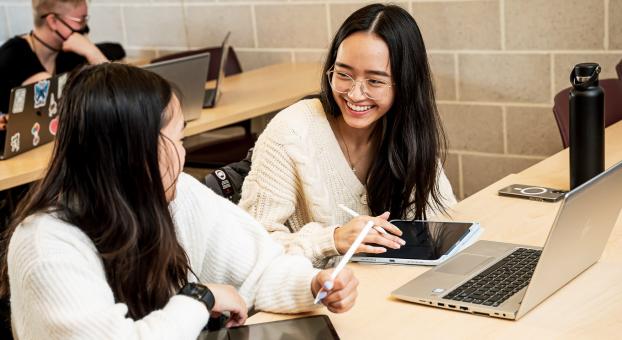 Dans une salle de classe de l'USB, deux étudiantes collaborent en toute complicité en utilisant des tablettes et un ordinateur portable.