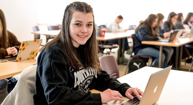 Une étudiante souriante travaille sur un ordinateur portable dans une salle de classe.