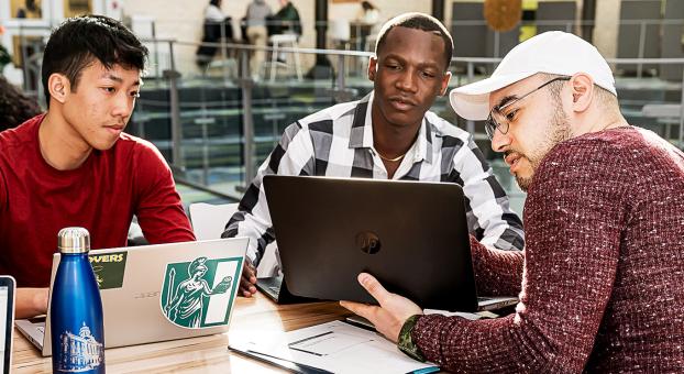 Trois étudiants utilisant des ordinateurs portables, travaillent ensemble dans un espace commun de l'USB.