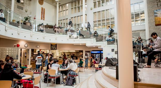 Le centre étudiant Étienne-Gaboury fourmillant d'activité, un musicien joue la guitare sur la scène.