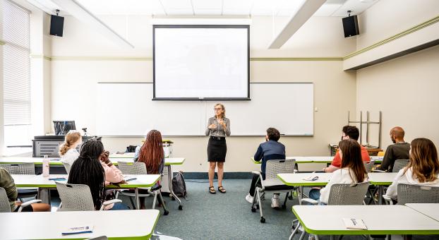 Une enseignante en salle de classe devant un groupe de personnes apprenantes.