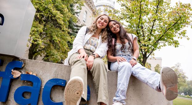 Deux étudiantes assisent sur le monument devant la façade de l'USB.