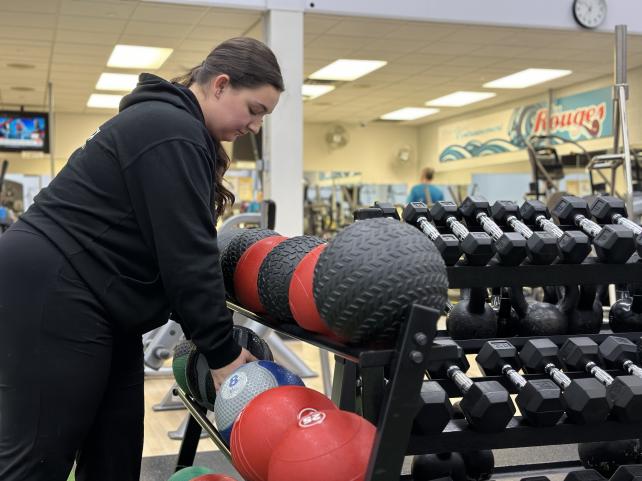 Une femme dans un centre de fitness sélectionne un ballon d'exercice parmi ceux disponibles sur un support pour haltères.