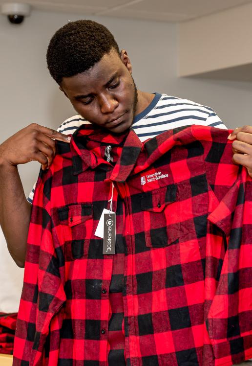 Un étudiant regarde une chemise carreautée rouge et noire à la Boutique.