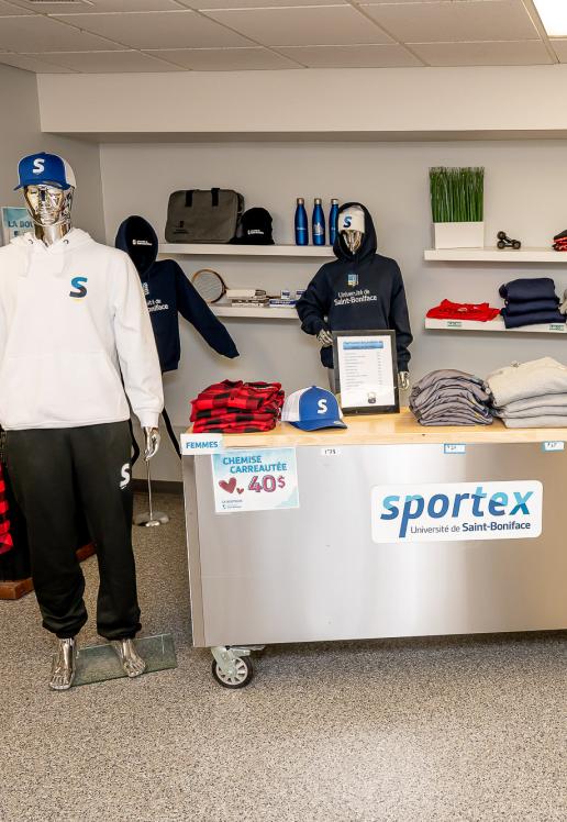 La Boutique avec plusieurs articles, comme des chemises, des bouteilles et des tuques, en exposition.