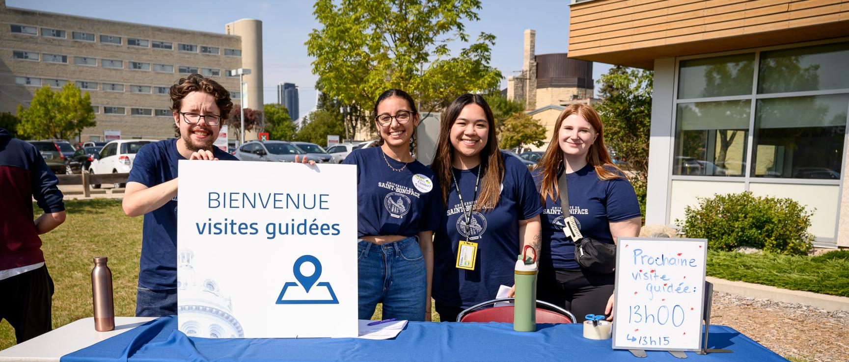 Groupe d’étudiants accueillants lors de la rentrée, avec une pancarte lisant« Bienvenue visites guidées » visible au premier plan.
