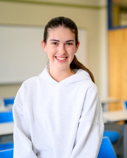 Dans une salle de classe, une jeune femme aux longs cheveux foncés attachés en queue de cheval sourit. 