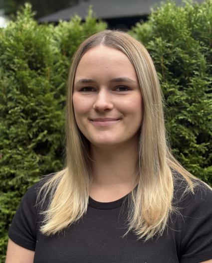 Une jeune femme aux long cheveux blonds portant un t-shirt noir sourit vers la caméra.