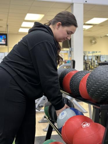 Une femme dans un centre de fitness sélectionne un ballon d'exercice parmi ceux disponibles sur un support pour haltères.