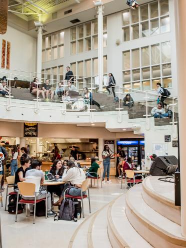 Le centre étudiant Étienne-Gaboury fourmillant d'activité, un musicien joue la guitare sur la scène.